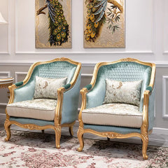 Pair of ornate armchairs with gold frames in a room with peacock artwork on the wall.
