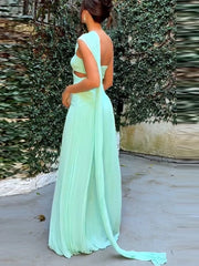 Woman wearing a light green evening gown with a long train, standing against a textured wall.