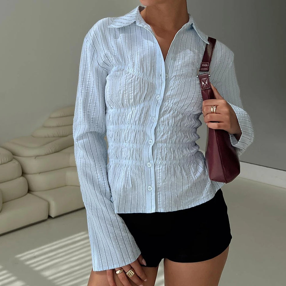 Person wearing a light blue textured shirt and black shorts, holding a maroon handbag indoors.