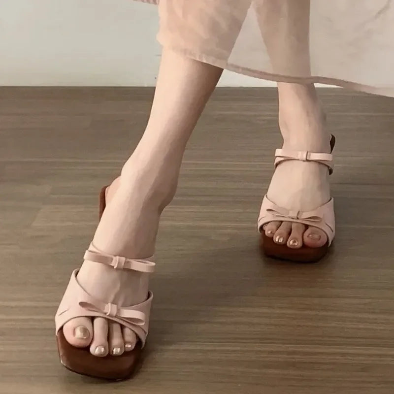 Pink sandals with brown soles worn by a person on a wooden floor.