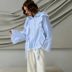 Woman wearing a light blue blouse with ruffled details against a neutral background