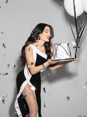 Woman in a black and white dress holding a cake against a gray background with balloons.
