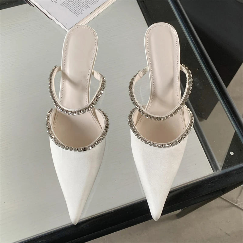 White pointed-toe shoes with rhinestone embellishments on a reflective surface.