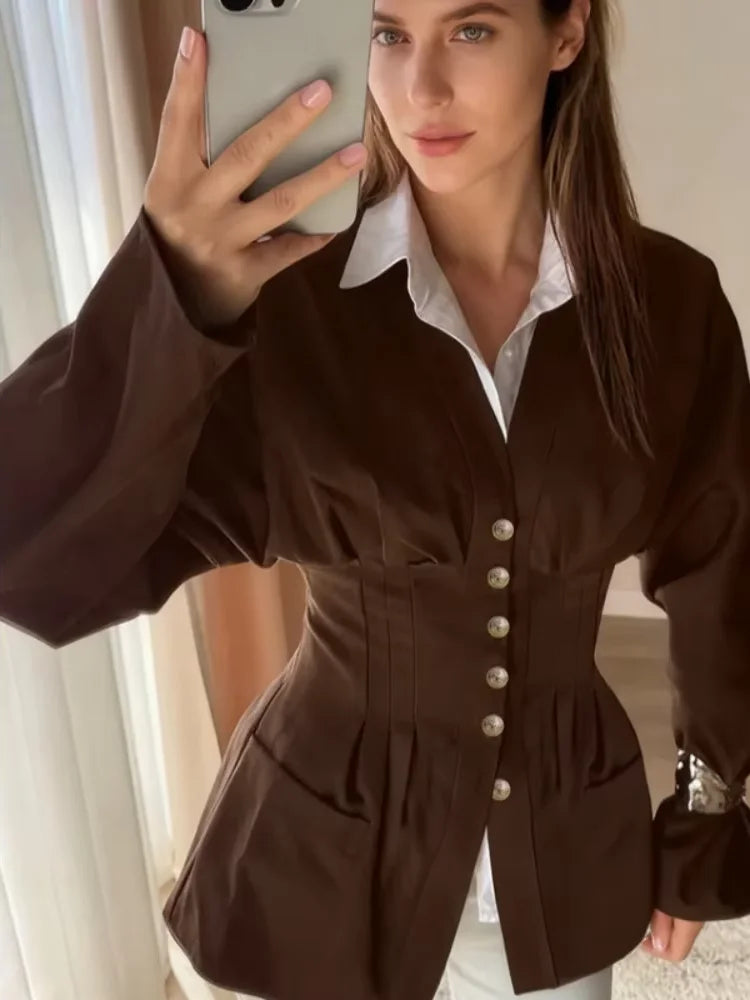 Woman taking a mirror selfie wearing a brown jacket with white buttons.