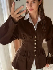 Woman taking a mirror selfie wearing a brown jacket with white buttons.