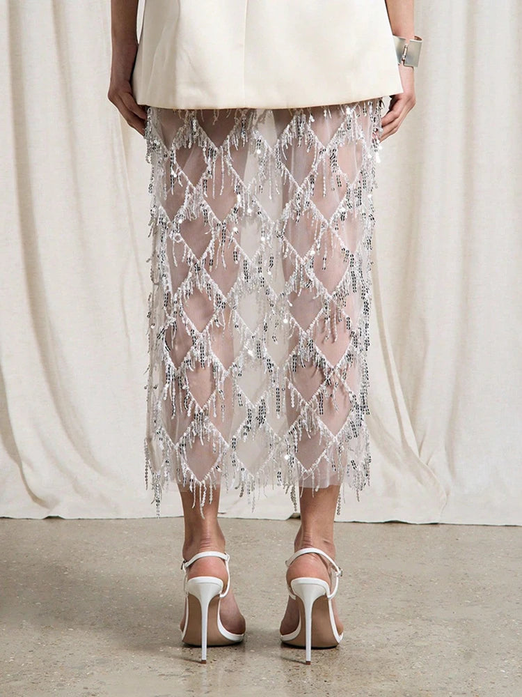 Person wearing a sheer beaded skirt with white high-heeled shoes on a neutral background