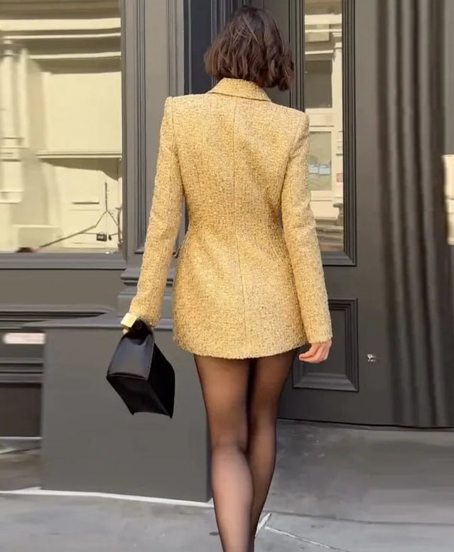 Woman in a yellow coat walking away from a building entrance.