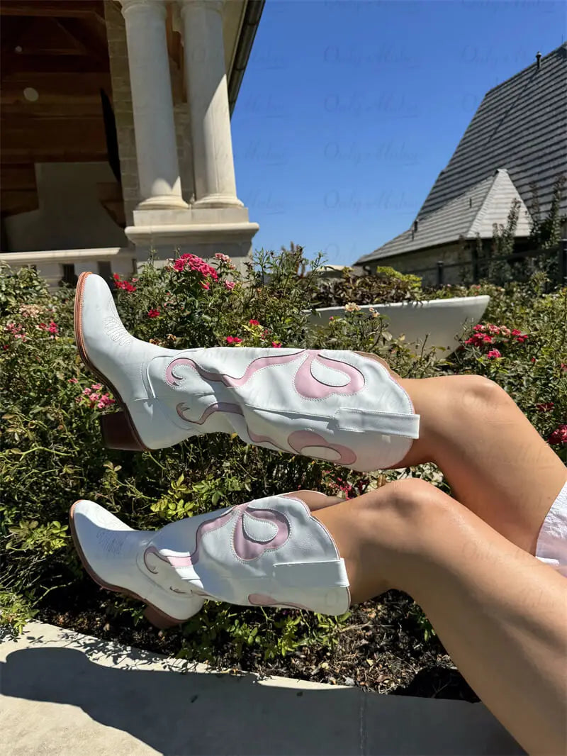 White cowboy boots with pink accents worn outdoors on a sunny day.