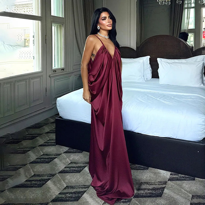 Woman in a burgundy dress standing in a bedroom with a bed and large windows.