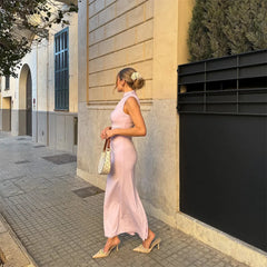 Woman in a pink dress standing on a sidewalk next to a building.