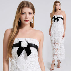 Woman wearing a white strapless dress with black bow and floral details on a plain background