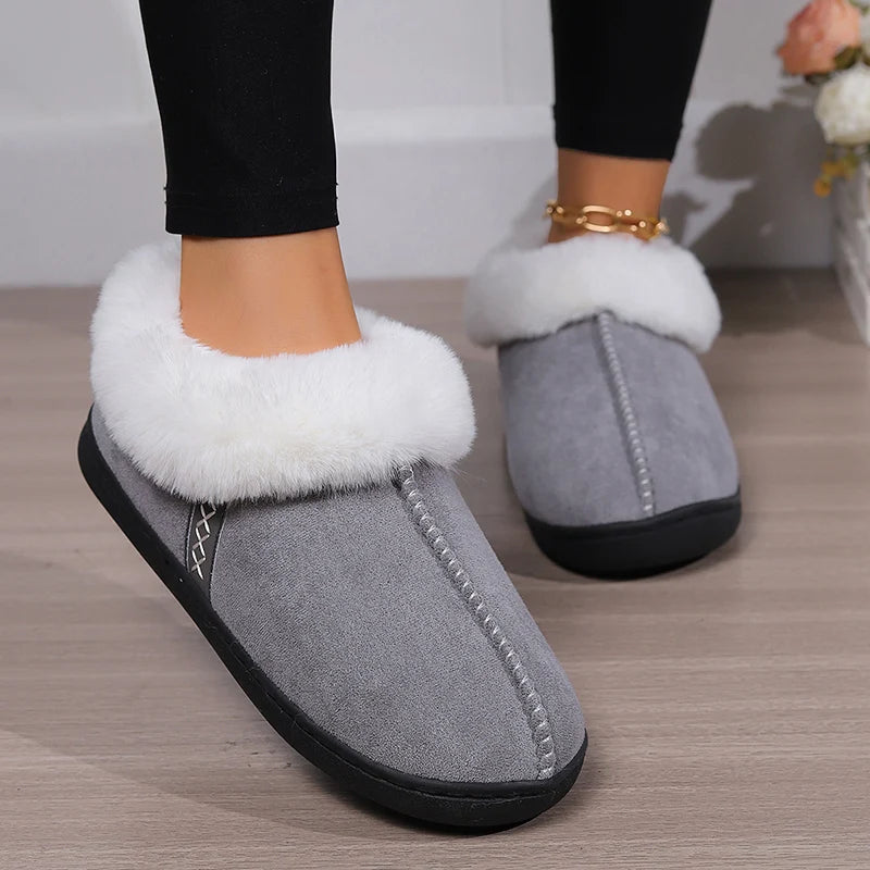 Gray slippers with white fur trim worn indoors on a wooden floor.