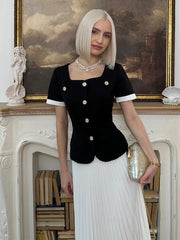 Woman in a black top with white trim and white skirt standing in an elegant room.
