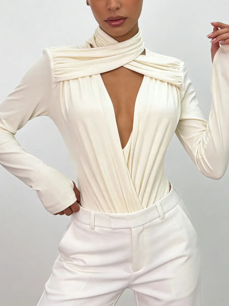 Person wearing an apricot long-sleeve top with a deep neckline and white pants on a light grey background