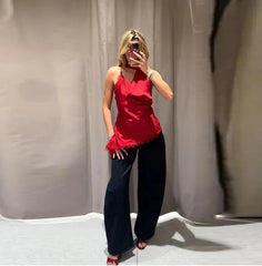 Woman taking a mirror selfie wearing a red top and black pants against a plain background