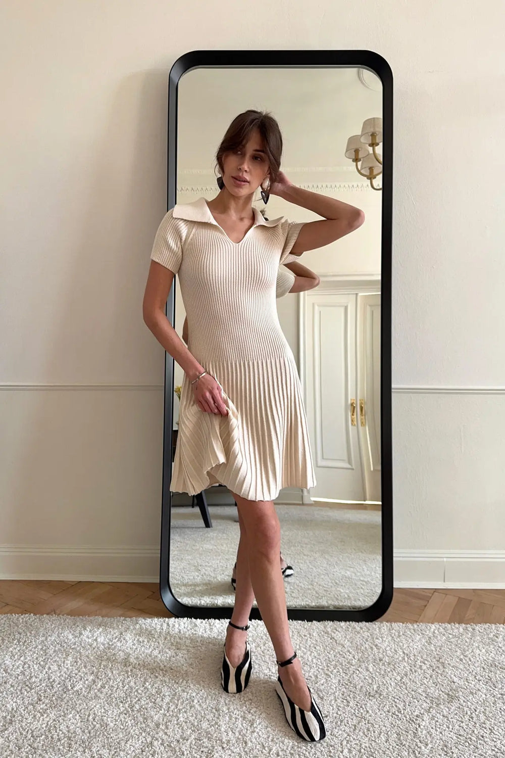 Woman in a cream dress standing in front of a full-length mirror.