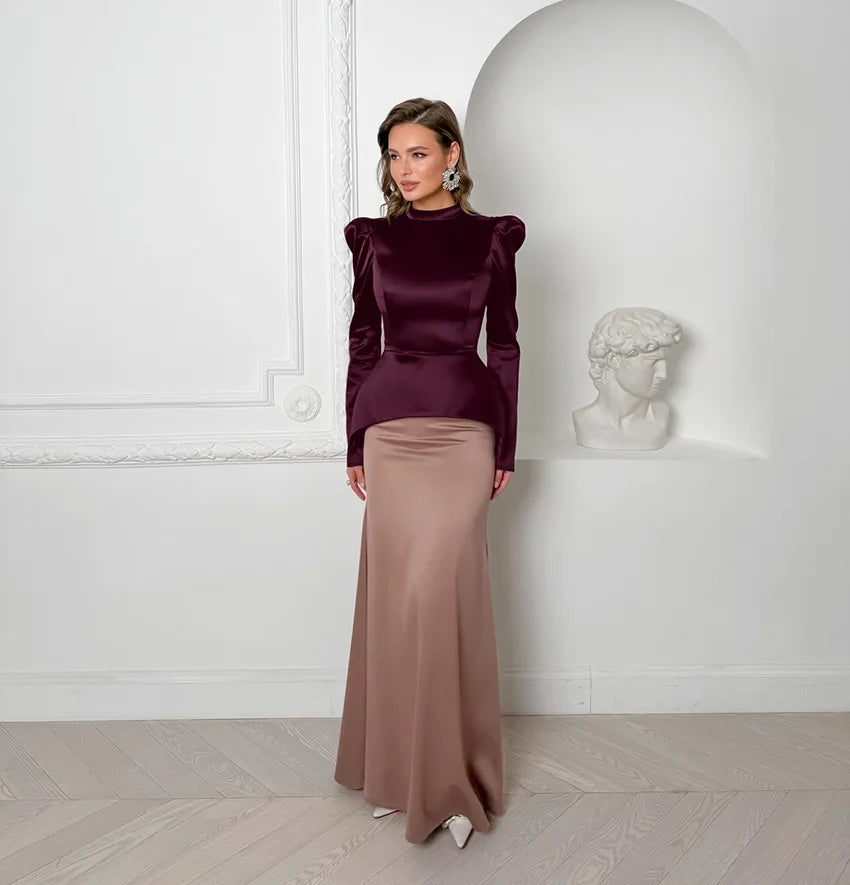 Woman in a burgundy top and beige skirt standing against a white wall with a classical bust.