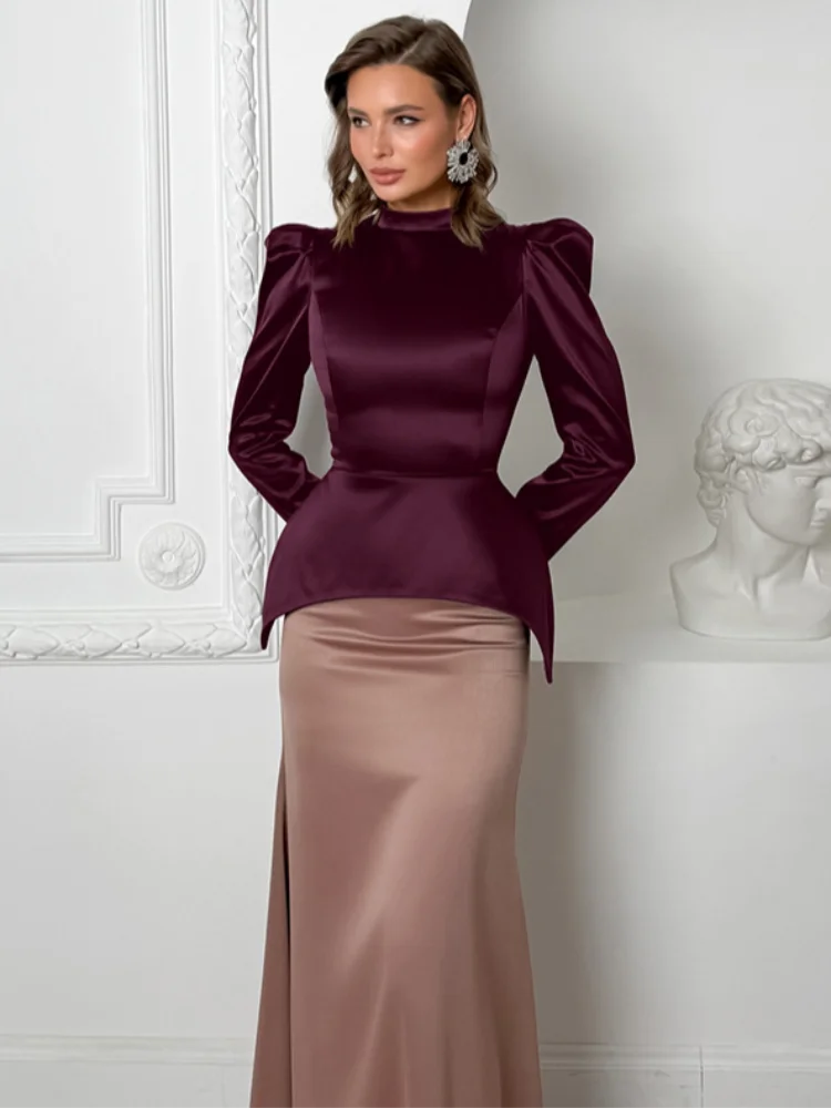 Woman wearing a burgundy top and beige skirt against a white wall.