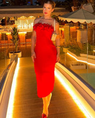 Woman in a red dress standing on a rooftop at night with a bar and outdoor furniture in the background.
