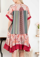 Woman wearing a colorful patterned dress with a white wall and chair in the background