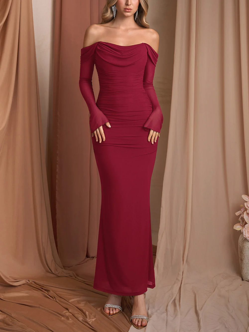 Woman wearing a burgundy off-shoulder gown against a beige curtain backdrop