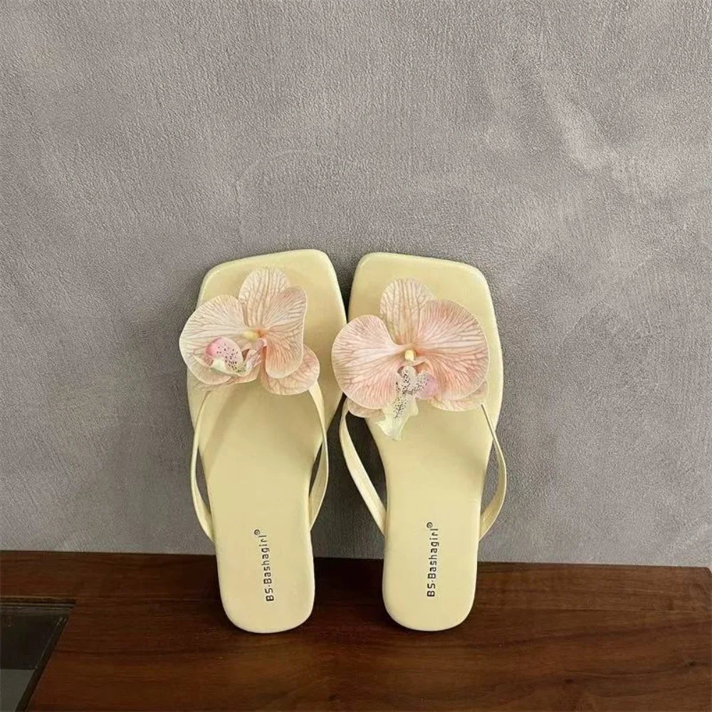 Pair of light yellow flip-flops with pink floral decorations on a gray background