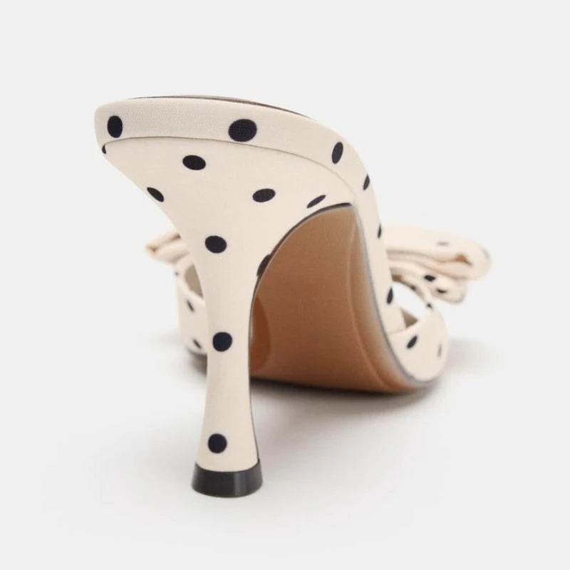 Beige high-heeled shoe with black polka dots on a white background