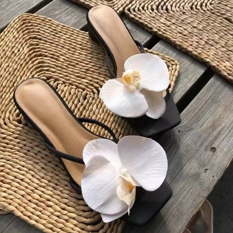 Black sandals with white orchids on a woven mat and wooden surface