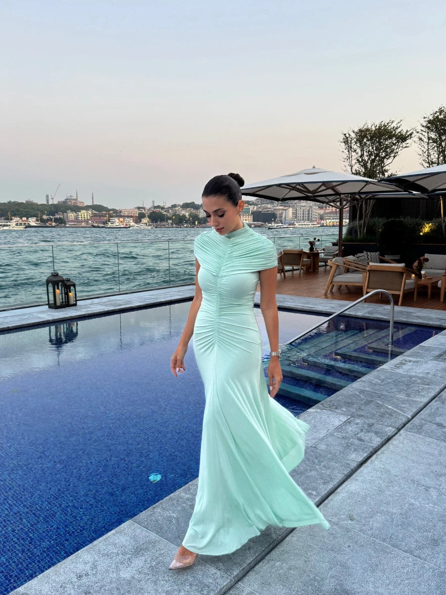 Woman in a light green dress standing by a pool with a cityscape in the background