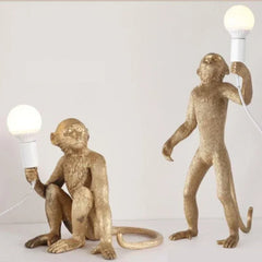 A playful retro monkey chandelier with three monkeys hanging from a branch, illuminating a modern coffee shop. 2  Bronze  Table Lamp