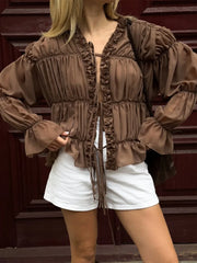 Person wearing a brown ruffled blouse and white shorts against a wooden staircase background
