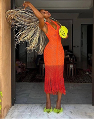 Woman in an orange dress with fringe holding a yellow bag in a room.