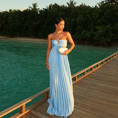 Woman in a light blue dress standing on a wooden deck by a body of water with greenery in the background.