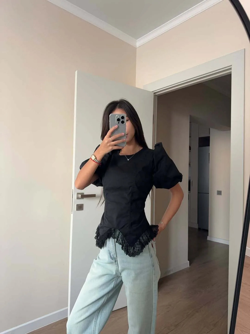 Person taking a mirror selfie wearing a black top and light blue jeans in a room.