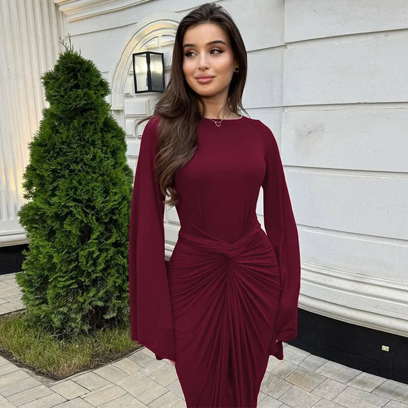 Woman in a burgundy dress standing outdoors next to a building.