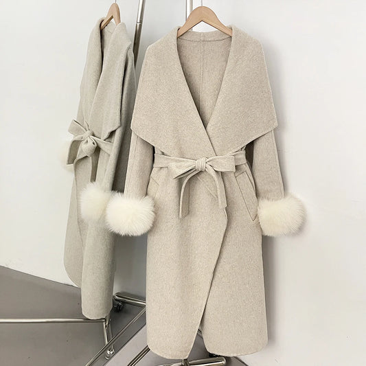 Beige wool blend coat with white fur trim and a belted waist.
