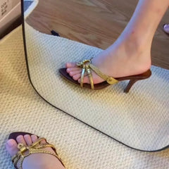 Gold high-heeled sandals with decorative straps on a textured surface.