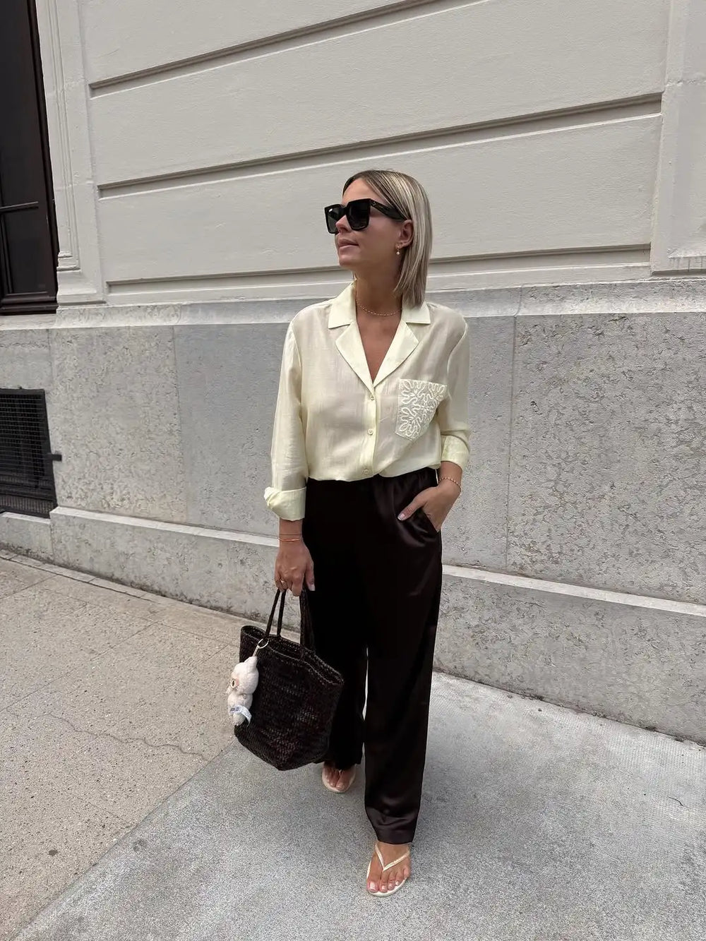 Woman in a cream blouse and black pants walking on a sidewalk.
