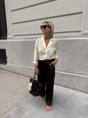 Woman in a cream blouse and black pants walking on a sidewalk.