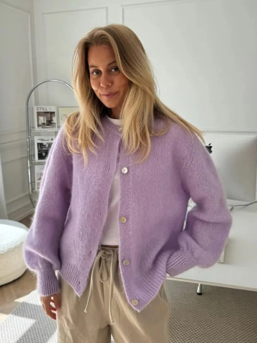 Woman wearing a purple cardigan in a room with white walls and furniture.