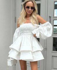 Woman wearing a white off-shoulder dress with puffed sleeves in front of a gray door.