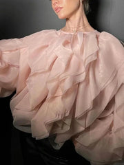 Close-up of a person wearing a light pink ruffled blouse against a dark background