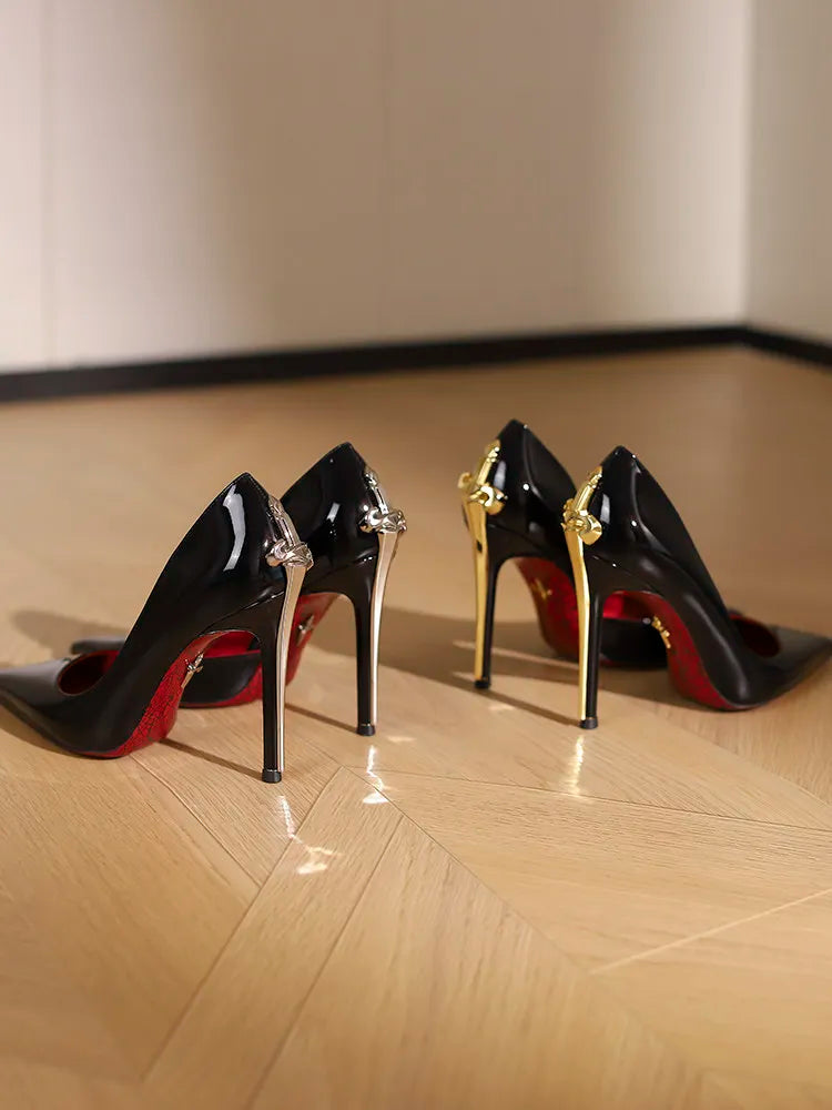 Pair of black high-heeled shoes with gold accents on a wooden floor.