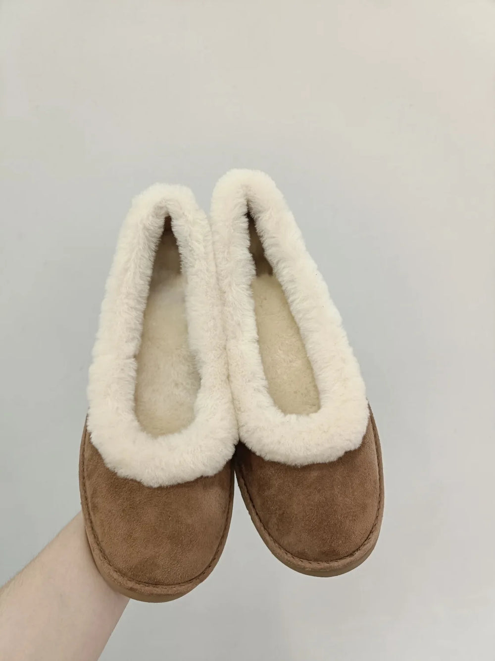 Pair of fleece lined slip on loafers held in hand
