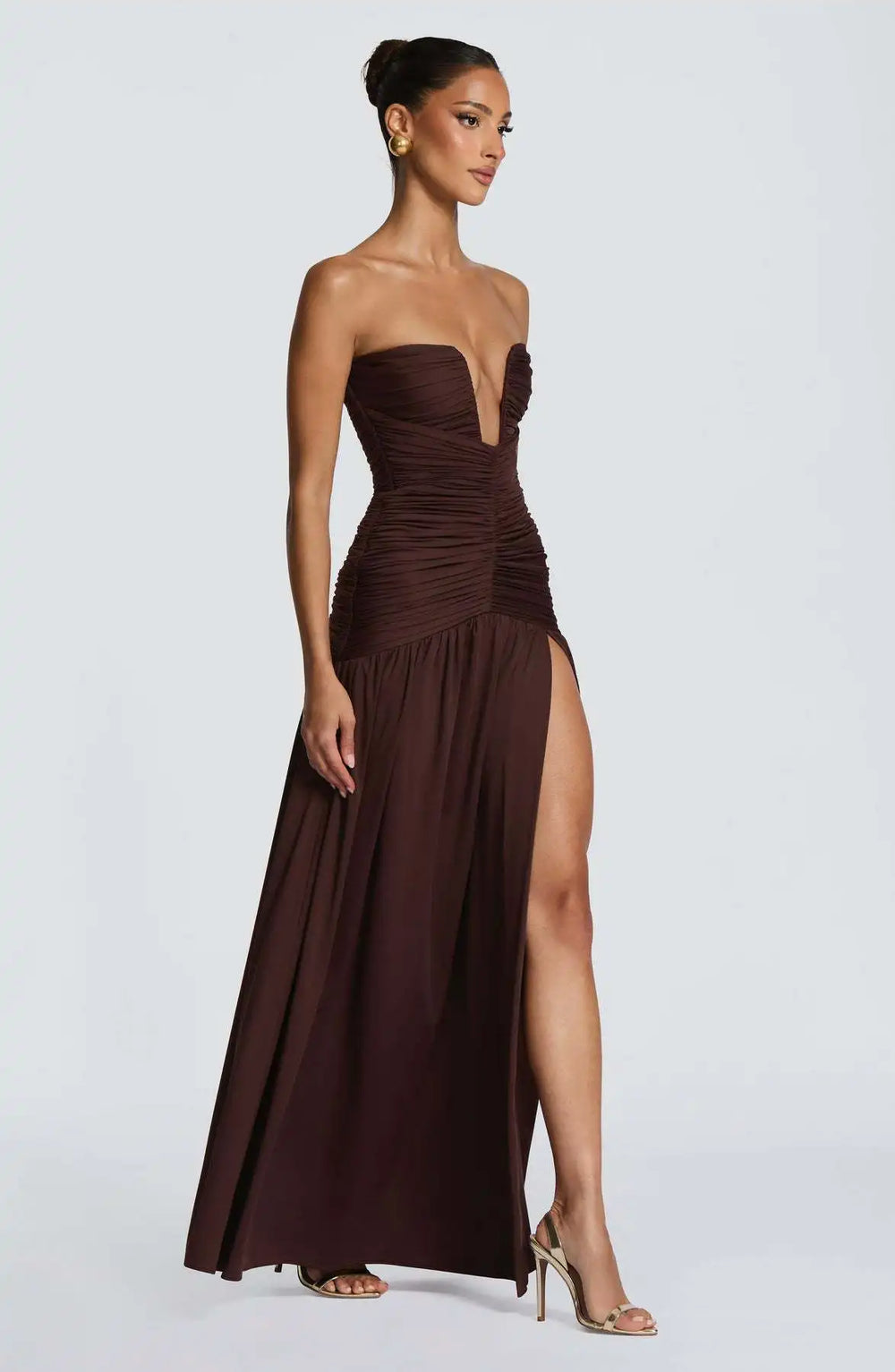 Woman wearing a strapless brown evening gown with a slit on a white background