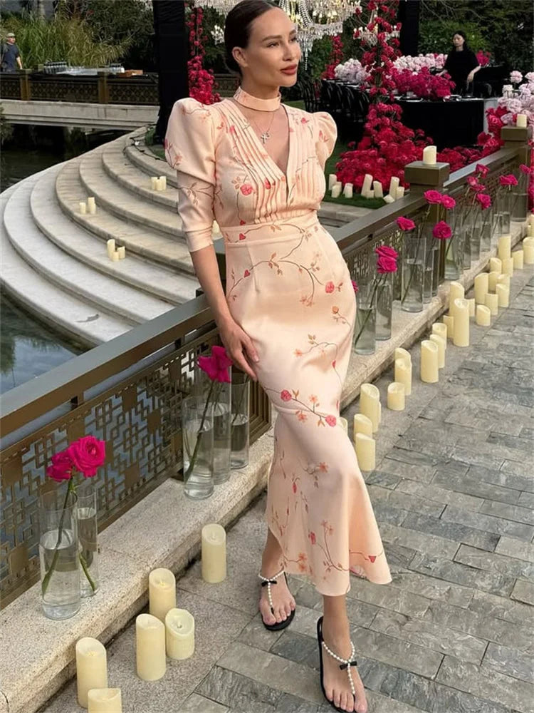 Woman in a floral dress standing by a decorative outdoor setting with candles and flowers.