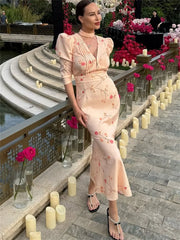 Woman in a floral dress standing by a decorative outdoor setting with candles and flowers.