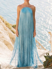 Front view of a strapless fringe maxi dress on a woman standing on a sandy path by the sea