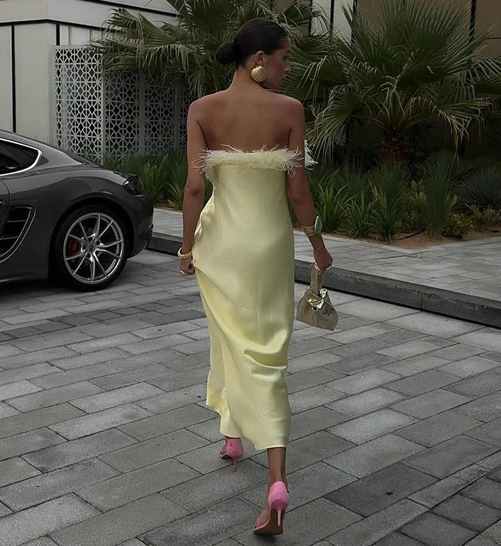 Woman in a yellow dress walking on a paved area with a car and plants in the background