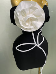 Black dress with a large white flower on a mannequin against a plain background